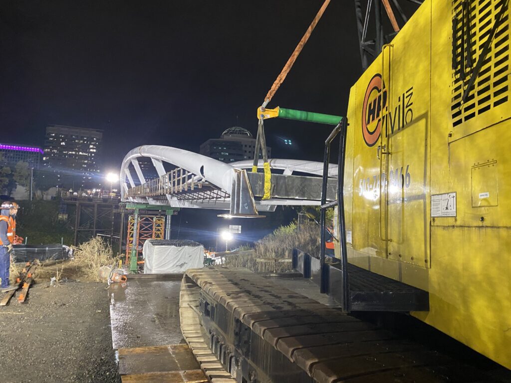 A yellow train is on the tracks near a bridge.